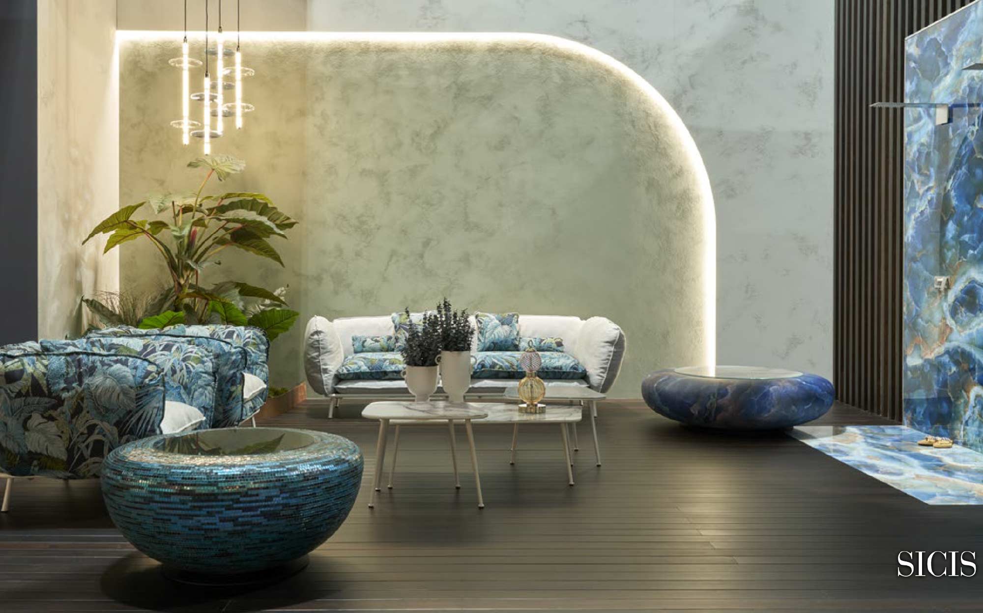 Tropical design and precious materials in Sicis wellness spaces | 101DOMUS Sicis relaxation area with tropical print armchairs and sofa, white coffee tables, and round mosaic and stone bathtubs